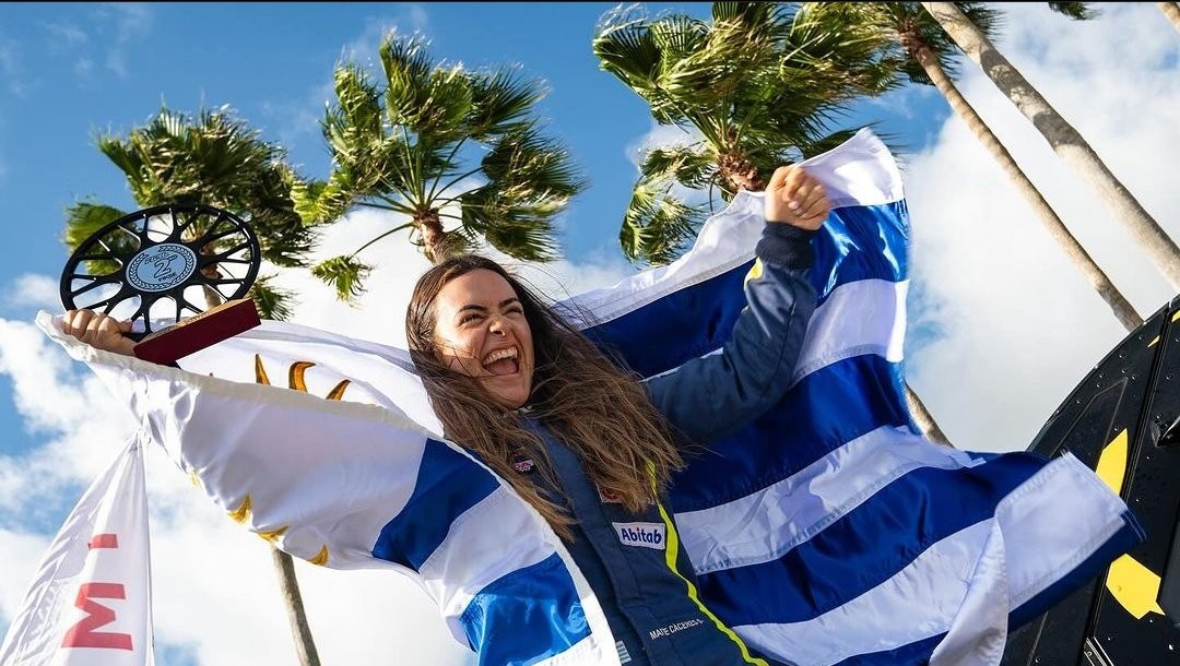 Maite Cáceres celebrating with a trophy, wrapped in the Uruguayan flag